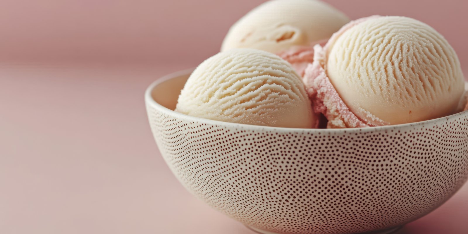 Delicious ice cream scoops served in a textured bowl against a soft pink backdrop